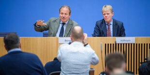 Frank Bsirske und Reiner Hoffmann sitzen nebeneinander hinter einem Tisch,im Vordergrund die Hinteransicht eines stehenden Fotografen