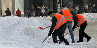 Drei Männer mit orangen Westen schaufeln Schnee