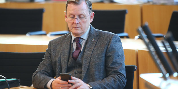 Bodo Ramelow sitzt im Plenarsaal des Thüringer Landtags und schaut auf sein Handy..