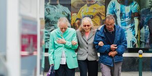 Dreii ältere Menschen laufen Arm in Arm durch die Straße