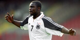 Gerald Asamoah, ein Mann mit dunkler Hautfarbe hat ein Deutschland-Trikot an und breitet beide Arme aus