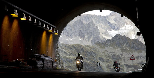 eine Tunnelöffnung mit Blick auf die Berge, Motorradfahrer rasen in den Tunnel