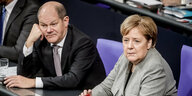Ein Mann und eine Frau, Olaf Scholz und Angela Merkel, sitzen in Anzügen nebeneinander