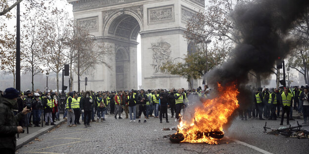 Demonstranten in gelben Westen scharen sich um einen brennenden Gegenstand in Paris