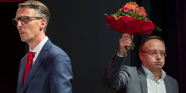 Zwei Männer, einer hebt einen Blumenstrauß hoch