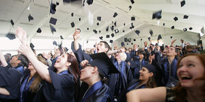 Studierende werfen ihre Hüte in die Luft.