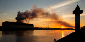 Eine Rauchschwade steigt aus einem Werft-Gebäude.