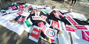 Demonstrant*innen liegen zwischen Schildern mit Namen von Modeketten
