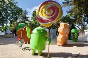 Einige bunte Google-Figuren stehen auf Sand, daneben ein Google-Fahrrad Einige bunte Google-Figuren stehen auf Sand, daneben ein Google-Fahrrad