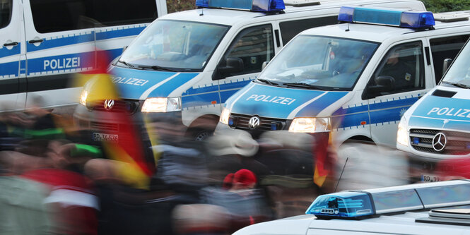 Deutschlandfahnen werden von Demonstranten hochgehalten, die zwischen Polizeiautos hindurchgehen.