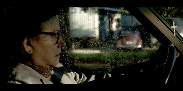Eine ältere Frau ist im Profil zu sehen, sie sitzt am Steuer eines Autos