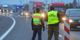 Autos stehen im Nebel am Grenzübergang nach Polen an, zwei Männer in gelben Westen sind von hinten zu sehen