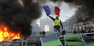 Ein Mann in einer gelben Warnweste steht neben eine brennenden Barrikade vor dem Triumphbogen in Paris