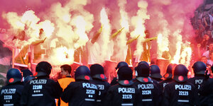 Brennende bengalische Feuer im Stadion, davor stehen Polizisten