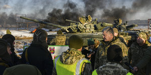 Ein Mann, Petro Poroschenko, spricht mit einer Gruppe von Soldaten, im Hintergrund ein Militärpanzer und viele dunkle Rauchschwaden