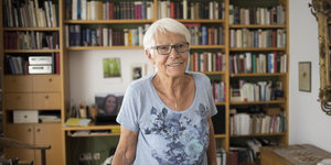 Eine ältere Frau vor einem Bücherregal blickt in die Kamera