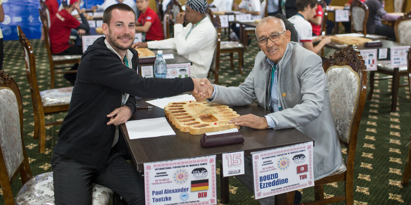 Zwei Männer reichen sich über einem Brettspiel die Hand