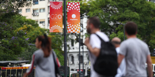 Menschen laufen in einer Stadt vor einem G20-Banner lang