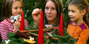 Eine Kita-Erzieherin zündet mit zwei Mädchen eine Kerze an einem Adventskranz an.