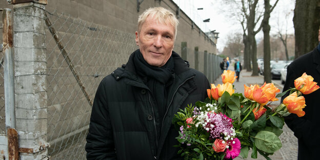 Ein Mann mit einem Blumenstrauß steht neben einer Mauer.