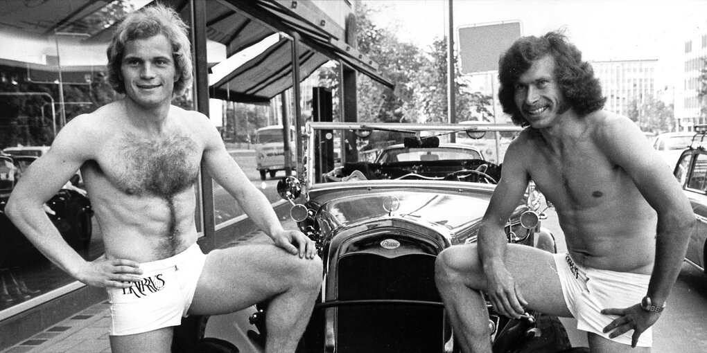 Uli Hoeneß und Paul Breitner nur mit Shorts bekleidet posieren vor einem Oldtimer