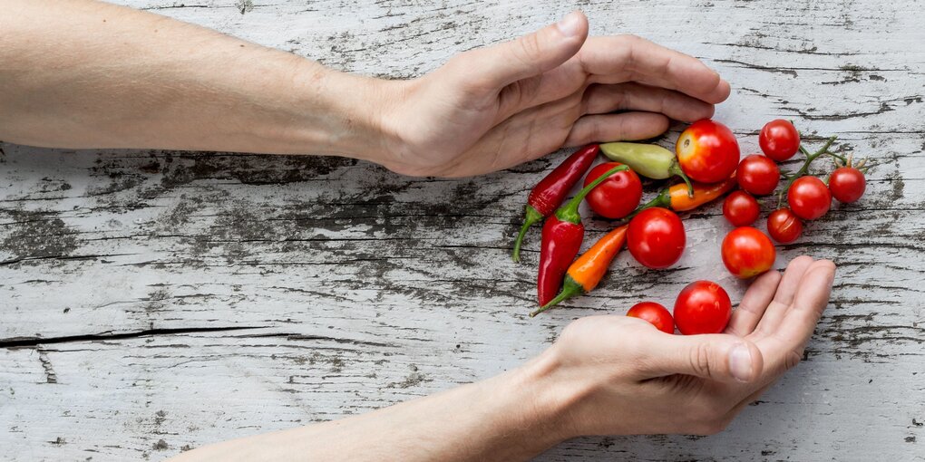 Paprika und Chilis auf einem weißen Tisch, von zwei Händen gerahmt