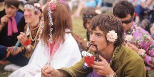 Auf einer Wiese sitzen bunt gekleidete Menschen mit Blumen in den Haaren