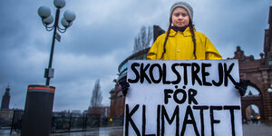 Ein junges Mädchen in gelbem Regenmantel hält ein Plakat mit der schwedischen Aufschrift "Schulstreik für das Klima"