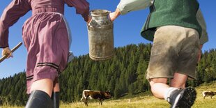 Zwei Landwirte laufen mit einer Milchkanne einer Kuh entgegen