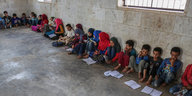 Kinder sitzen nebeneinander in einer provisorischen Schule auf dem Boden