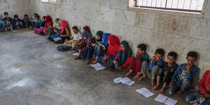 Kinder sitzen nebeneinander in einer provisorischen Schule auf dem Boden
