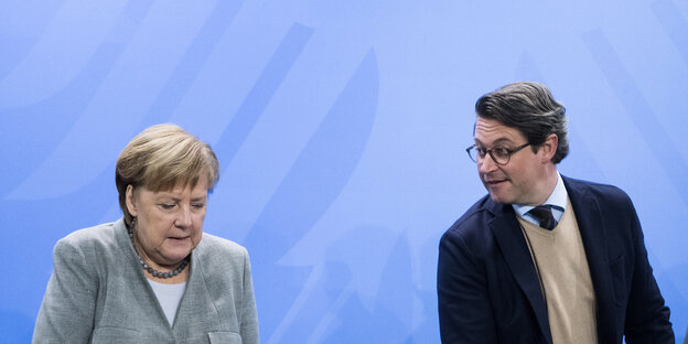 Angela Merkel und Andreas Scheuer stehen nebeneinander vor einer blauen Wand