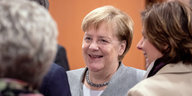 Angela Merkel lächelt, umgeben von anderen Personen