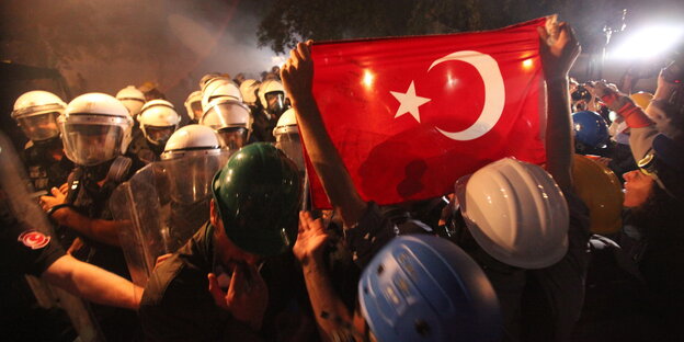 Demonstranten und Polizisten – einer der Demonstranten hält eine Türkeiflagge in die Höhe