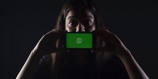 Frau hält Smartphone mit Whatsapp-Symbol vor ihren Mund