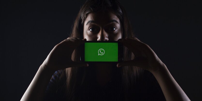 Frau hält Smartphone mit Whatsapp-Symbol vor ihren Mund