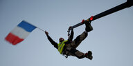 Mann in Gelber Weste schwingt eine Frankreichfahne in hoher Luft