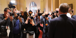 Ein Mann steht mit dem Rücken zum Betrachter und wird von vielen Fotografen abgelichtet