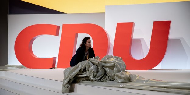 Drei große rote Buchstaben CDU und eine Frau vor einer Abdeckfolie