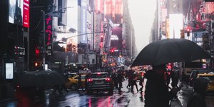 Menschen in New York überqueren eine Straße, es regnet, sie tragen Schirme