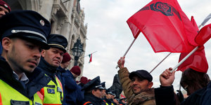Ein Mann steht neben zwei Polizisten und hält eine rote Flagge in die Luft