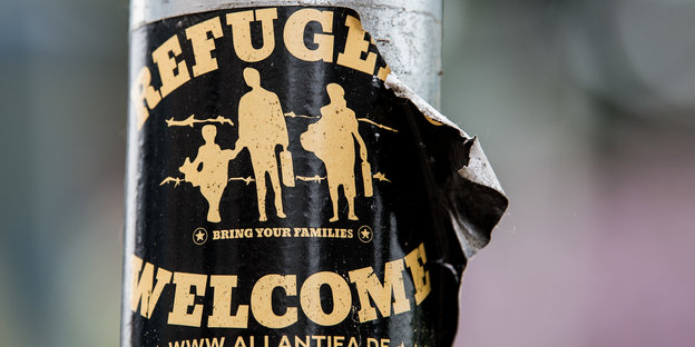 Ein Aufkleber mit der Aufschrift Refugees welcome an einer Stange