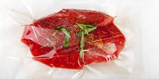 Ein in Plastikfolie verpacktes Stück Fleisch mit ein wenig frischen Gewürzen