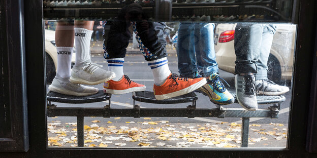 Durch ein Fenster einer Busstation sieht man die Schuhe von fünf Menschen.