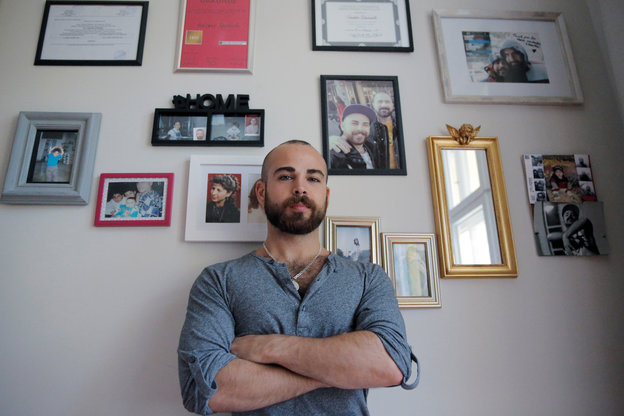Ein Mann steht vor einer Wand voller Fotos von Freunden und Familie