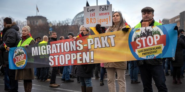 Menschen protestieren mit Plakaten gegen den UN-Migrationspakt