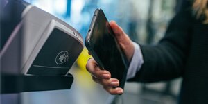 So kann Apple Pay aussehen: Eine Person hält ein Smartphone vor ein Bezahlterminal