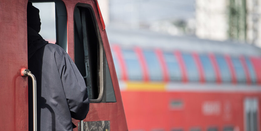 Ein Lokführer steht im Bahnhof an der Tür zu einem Führerstand