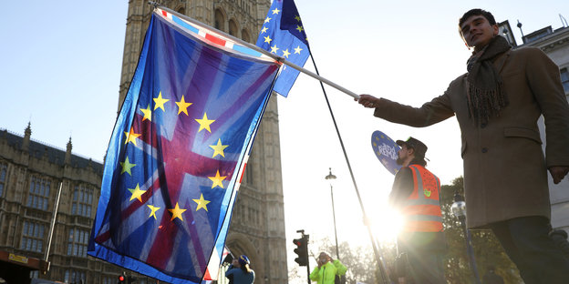 Ein Mann hält in der Abendsonne die britische und die europäische Flagge übereinander