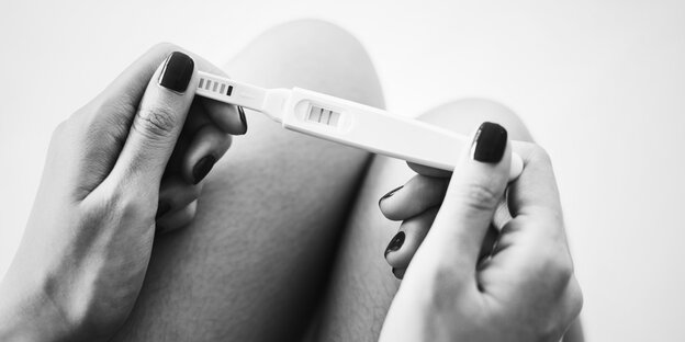 Eine Frau hält einen positiven Schwangerschaftstest in den Händen